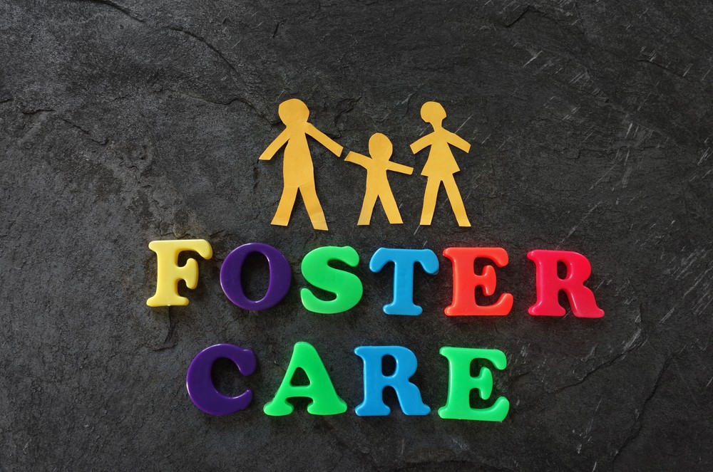 Fridge letter magnets that spell "foster care" with a set of parents and a child holding hands above